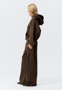 Bruine oversized hoodie met trekkoorden en een buidelzak, gecombineerd met bijpassende wijde broek met een reliëfpatroon. Getextureerde stof.