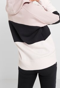 Felpa con cappuccio color block in rosa chiaro, nero e crema. Caratterizzata da un tessuto morbido, cappuccio e polsini a coste, con una vestibilità rilassata.