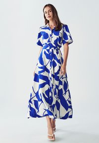 Maxi šaty vyrobené z lehkého materiálu, s modro-bílým vzorem listů, krátkými rukávy, límečkem, knoflíkovým zapínáním a zavázaným pasem.