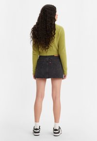 Groene fluffy cropped trui, zwarte denim mini rok met een rafelige zoom, witte sokken en twee-kleurige sneakers, gezien van achteren.