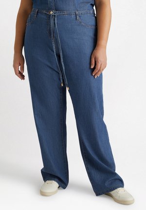 Blauwe denim wijde broek met een tailleband met trekkoord en goudkleurige accenten. Voorzien van steekzakken en een comfortabele pasvorm. G gedragen met witte sneakers.