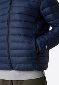 Giubbotto imbottito blu navy con sezioni trapuntate, chiusura con zip anteriore e orlo regolabile. Dotato di accessori neri e logo sul polsino.