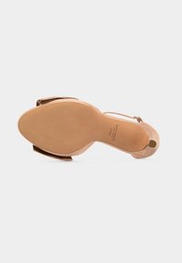 Μπεζ πέδιλο με ψηλό τακούνι, μυτερή μύτη, λουράκι στον αστράγαλο με αγκράφα και λείο πέλμα που δείχνει το όνομα της μάρκας και το μέγεθος 7.5B.