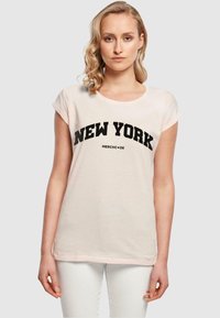 Kerge roosa puuvillane T-särk rullitud lühikeste varrukatega ja ümmarguse kaelusega. Esiküljel on julged mustad "NEW YORK" tähed.