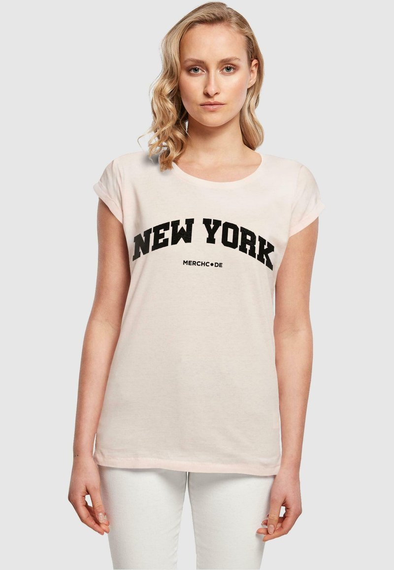 Kerge roosa puuvillane T-särk rullitud lühikeste varrukatega ja ümmarguse kaelusega. Esiküljel on julged mustad "NEW YORK" tähed.