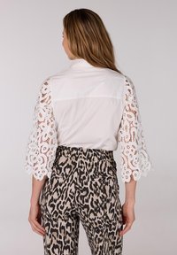 Witte blouse met kant mouwen, gecombineerd met een broek in leopardenprint met een aangesloten taille en achterzakken. Gladde stof en textuur contrasteren.