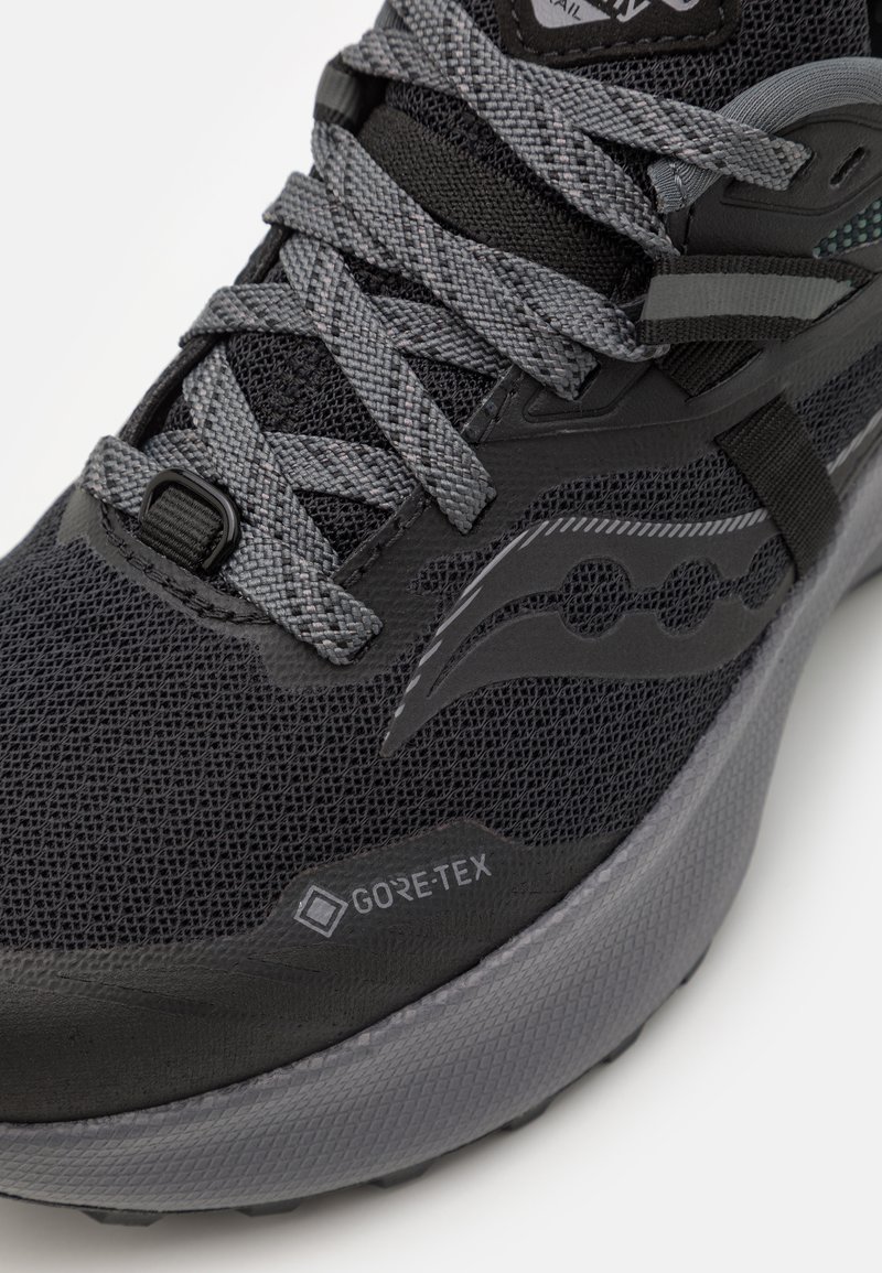 Zapatilla de running negra con parte superior de malla texturizada, cordones grises y una suela acolchada con la marca GORE-TEX. Diseño duradero y ligero.