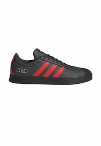 Baskets noires avec accents rouges, trois bandes caractéristiques, une semelle en caoutchouc noir texturée et un logo sur le côté. Matériau synthétique lisse.