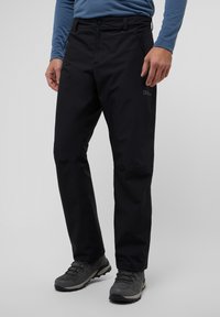 Zwarte outdoorbroeken van waterdicht materiaal met ritszakken en een recht model, gecombineerd met grijze wandelschoenen.