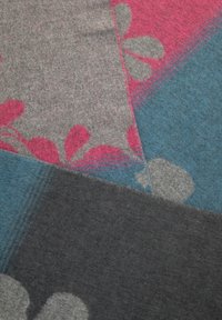 Couverture en laine multicolore avec des sections grises, roses et bleues, ornée de motifs floraux et d'une texture douce. Les bords sont soigneusement cousus.