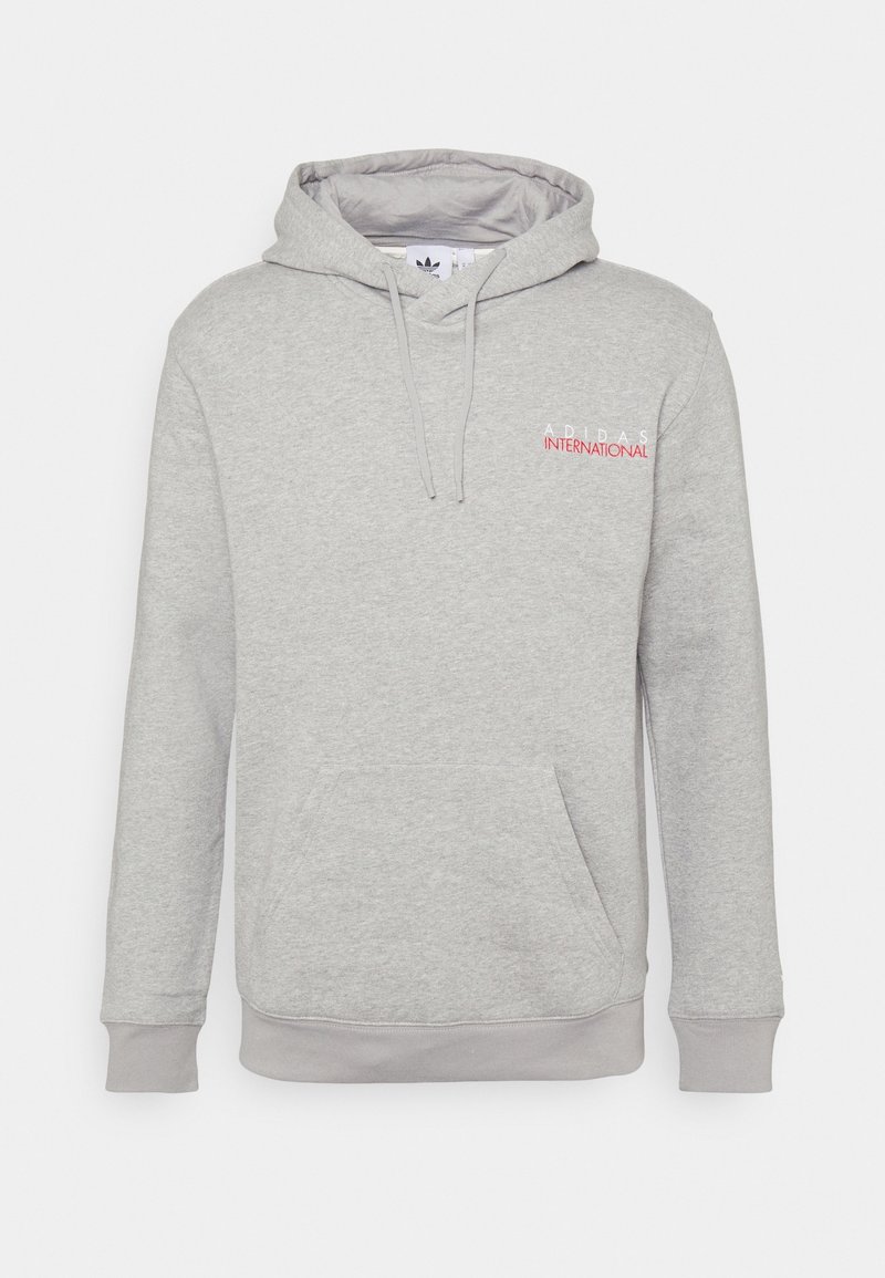 Šedá mikina s kapucí vyrobená z fleecového materiálu. Obsahuje přední klokánkovou kapsu a červené logo "ADIDAS INTERNATIONAL" na hrudi.