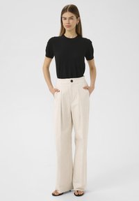 Black short-sleeve top paired with high-waisted, cream wide-leg trousers featuring a front button and pleats, placed on a neutral background.