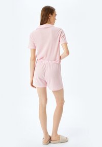 Conjunto de polo rosa de manga corta y pantalones cortos, textura acanalada, cinturilla elástica, diseño sencillo. Modelo lleva zapatillas beige.