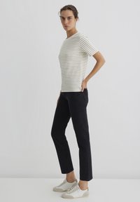 Gestreiftes kurzärmliges T-Shirt in Creme und Beige, kombiniert mit dunklen Jeans und hellen Sneakers. Schlichtes Design mit lässiger Passform.