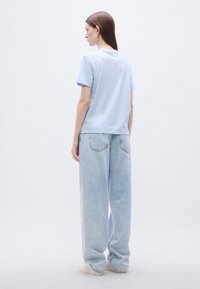 Ανοιχτό μπλε βαμβακερό T-shirt με κοντά μανίκια, σε συνδυασμό με ανοιχτό μπλε τζιν παντελόνι με φαρδιά μπατζάκια. Το ύφασμα είναι μαλακό με λεία υφή.