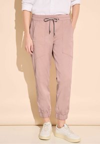 Light pink elastic waist pants with drawstring, side pockets, and elastic cuffs, paired with white sneakers on a neutral background.