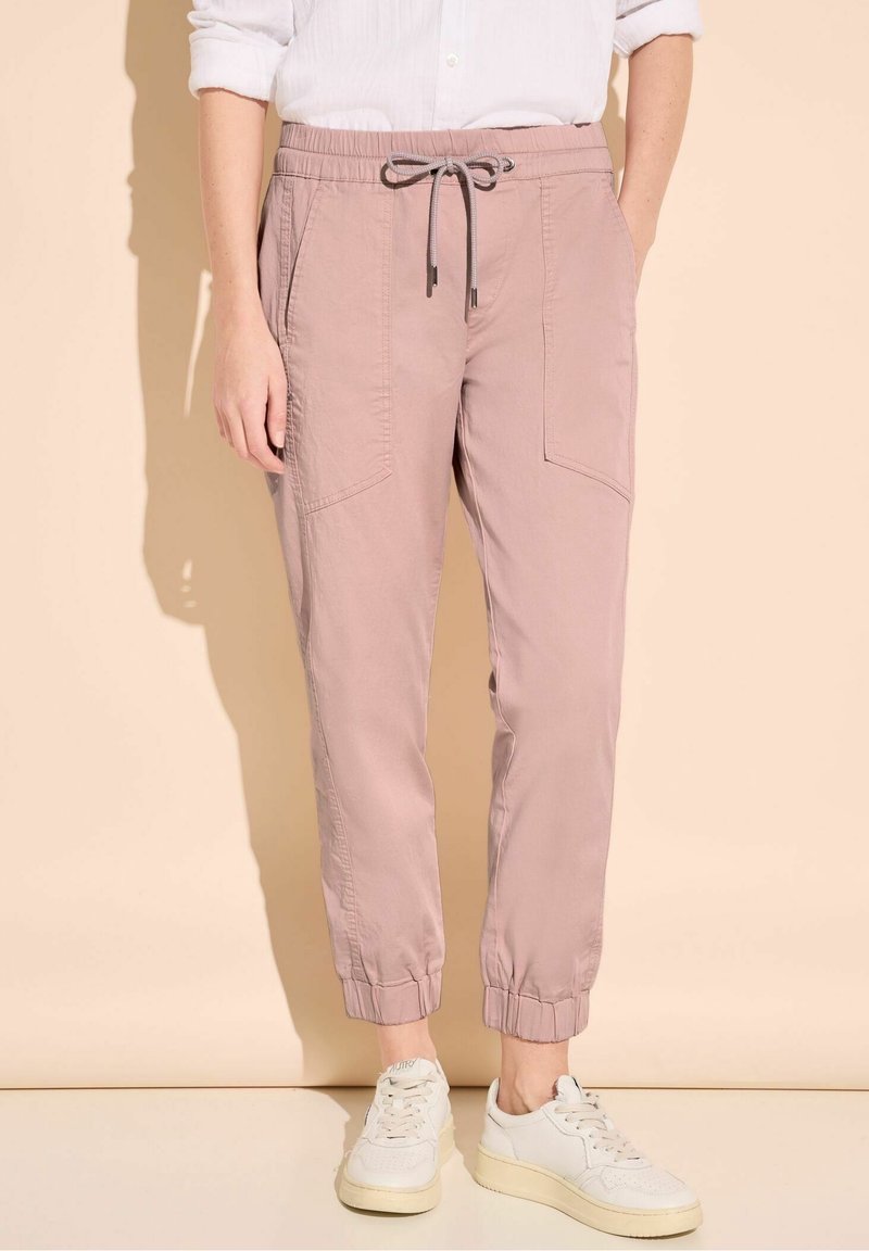 Light pink elastic waist pants with drawstring, side pockets, and elastic cuffs, paired with white sneakers on a neutral background.