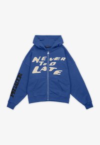 Sudadera azul con cremallera hecha de un tejido suave. Presenta "NUNCA ES TARDE" impreso en blanco en la parte delantera, con "PECADOR" impreso en negro en la manga.