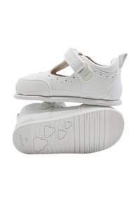 Zapatos de cuero blancos con detalles perforados, puntera redondeada y una correa de Velcro. La suela presenta un patrón de corazones y un agarre texturizado.