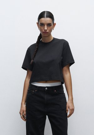 Zwarte cropped t-shirt met korte mouwen, gemaakt van zacht katoen. Gecombineerd met high-waisted zwarte jeans met een knoopsluiting en een witte tailleband.