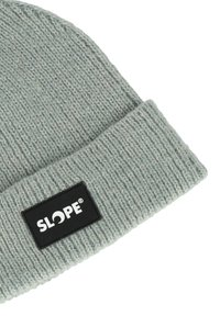 Harmaa neulottu beanie, jossa on käännetty reuna ja musta suorakulmainen etiketti, jossa lukee "SLOPE" valkoisella. Pehmeä rakenne, rento muotoilu.