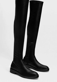 Botas negras hasta la rodilla hechas de cuero suave, con punta redonda, suela plana y cremallera lateral para facilitar el uso.