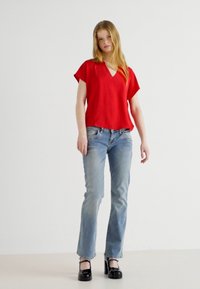 Red, short-sleeve top with a V-neck, paired with light blue jeans and black platform heels. Smooth fabric with a relaxed fit.