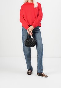 Sweat-shirt rouge, jean taille haute bleu, sac à main matelassé noir et ballerines imprimé léopard. Design minimaliste avec des couleurs et des textures contrastées.