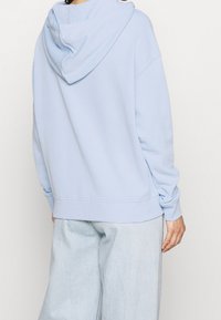 Sudadera azul claro con capucha de doble capa, puños y bajo acanalados, con un ajuste relajado y una textura suave.