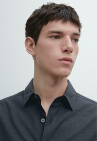 Donkergrijs overhemd met kraag en knoopsluiting. Gladde, getextureerde stof met subtiele stikseldetails en standaard knoopsluiting.