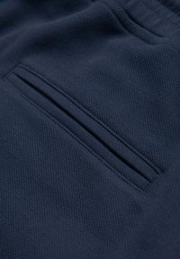 Gros plan d'un tissu bleu marine texturé avec une poche à fente horizontale bordée de coutures propres et étroites.