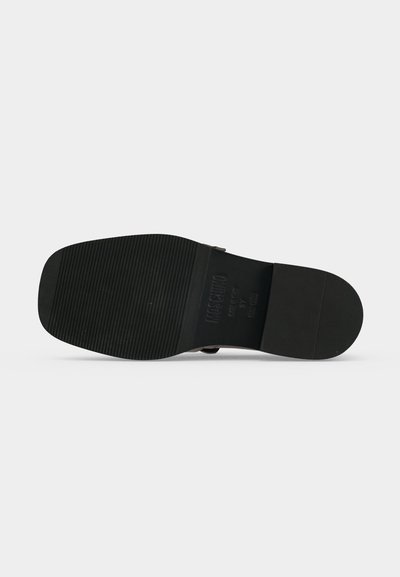 Semelle de chaussure noire avec motif de bande de roulement rainuré sur la moitié avant et talon lisse, vue de dessous sur un fond gris clair.