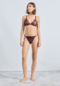 Bralet din dantelă și thong asortat, de culoare burgundă închisă. Prezintă modele florale intricate, bretele ajustabile și margini delicate cu dantelă.