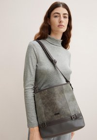 Graue Lederhandtasche mit strukturiertem Finish, featuring einen dunkleren unteren Bereich und Schnallenakzenten, über die Schulter getragen mit einem Riemen.