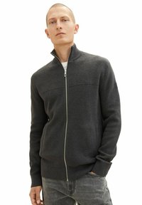 Szary sweter zapinany na zamek z wysokim kołnierzem, prążkowaną teksturą na ramionach i gładkim korpusem. Posiada boczne kieszenie i mankiety.