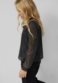 Zwarte, glanzende top met lange mouwen en een losse pasvorm, met verkwikte polsen, een hoge halslijn en doorzichtig textuurstof.