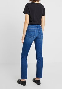 Jeans de mezclilla azul con un ajuste slim y una cintura de altura media, que cuentan con bolsillos traseros y una textura suave. Combinados con una camisa negra de manga corta.