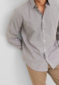 Brun och vit rutad skjorta med knäppning på kragen, långa ärmar och subtil textur; parat med ljusbruna byxor.