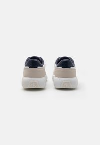 Witte en beige sneakers met een gestructureerde bovenkant, marineblauwe accenten, een gevoerde hak en een gestreepte rubberen zool.