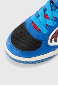 Blauwe sportieve schoen met een zwarte getextureerde neuskap, rode accenten bij de veters en blauwe veters; bevat witte en zwarte patroondetails.