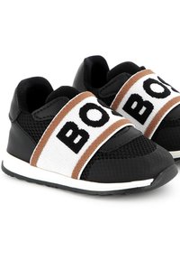 Black athletic shoes featuring a breathable mesh upper, elastic white and brown strap, and textured rubber sole with white trim.