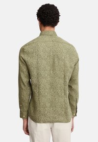 Grüne Hemdbluse mit floralem Muster, langen Ärmeln und Kragen; weist eine dezente Textur und goldfarbene Knöpfe an den Manschetten auf.