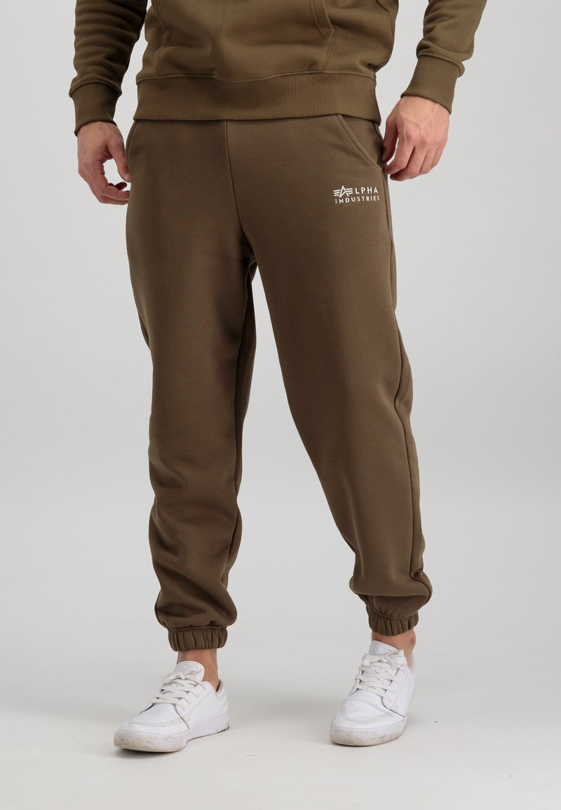 Olivno zeleni športni hlače iz mehke tkanine, z elastičnim pasom in manšetami, z belim logotipom "Alpha Industries" na stegnu.