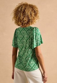 Zaļš īsām piedurknēm krekls ar ziedu paisley rakstu un savilktām plecu daļām. Viegls audums ar gludu faktūru. Stilizēts ar baltām biksēm.