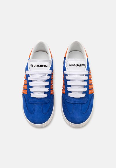 Zapatillas de ante azul con cordones blancos y detalles en naranja. Presentan un panel lateral de malla y un logo en la lengüeta. Suela de goma plana.