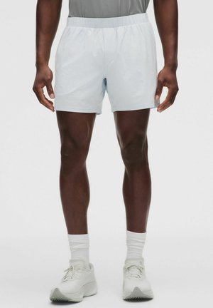 Mand iført hvide atletikshorts, hvide sokker og hvide løbesko, stående mod en ensfarvet lys baggrund.