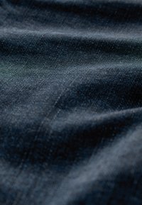 Detail tmavomodrej rifľoviny zobrazujúci textúru a jemné záhyby pod mäkkým svetlom.