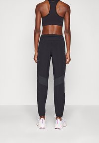 Svart träningsoutfit som inkluderar en sport-bh med racerback och tapered byxor med reflexdetaljer, ankelflärpar och sidofickor med blixtlås.