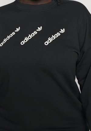 Czarna koszula z długim rękawem z trzema ukośnymi białymi logo Adidas i symbolami koniczyny na górnej części klatki piersiowej.