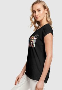 Sort t-shirt med korte ærmer, der har et grafisk design af ansigtter og tekst på fronten. Lavet af blødt, åndbart stof.